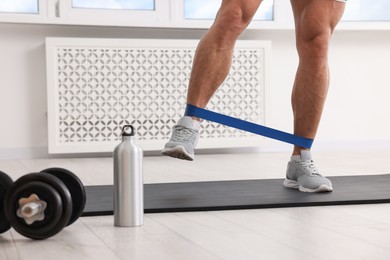 Photo of Athletic man doing exercise with elastic resistance band on mat indoors, closeup