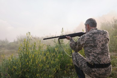 Man wearing camouflage and aiming with hunting rifle outdoors, back view. Space for text
