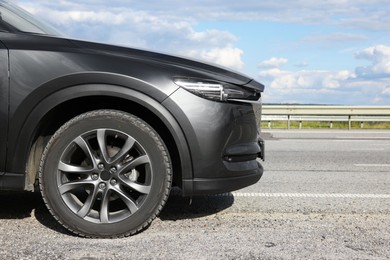 Photo of New black modern car on asphalt road, closeup. Space for text