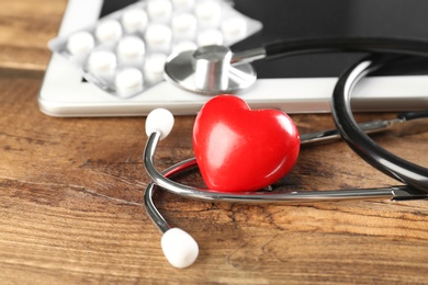 Photo of Stethoscope and small red heart on wooden table. Heart attack concept