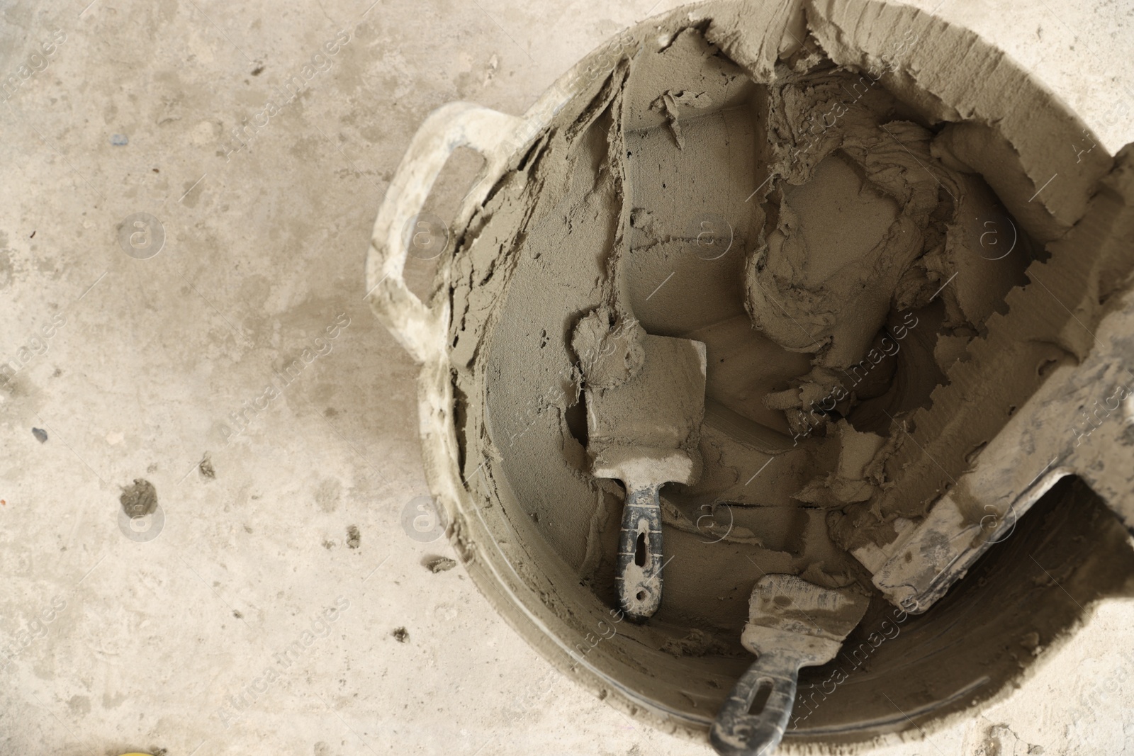 Photo of Bucket with cement and putty knifes on floor, top view. Space for text