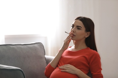 Photo of Young pregnant woman smoking cigarette at home. Space for text