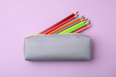 Many colorful pencils in pencil case on pink background, top view