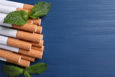 Photo of Menthol cigarettes and mint leaves on blue wooden table, flat lay. Space for text