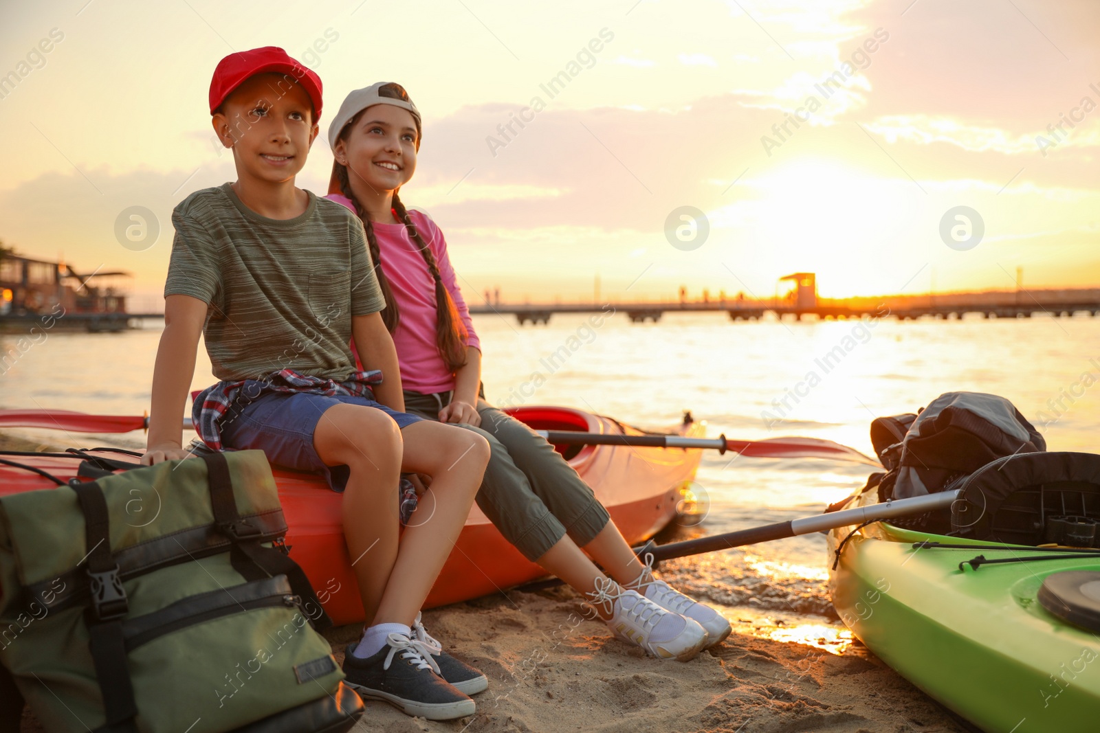 Photo of Happy children sitting on kayak near river at sunset. Summer camp