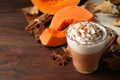 Photo of Delicious pumpkin latte and ingredients on brown wooden table, closeup. Space for text