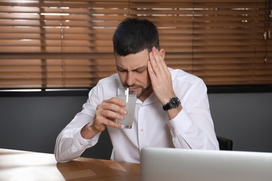 Photo of Man taking medicine for hangover at desk in office