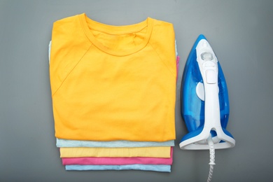 Folded clean clothes and iron on color background, top view