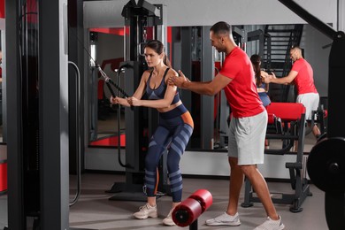 Trainer explaining woman how to do exercise properly in modern gym, space for text