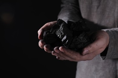 Photo of Man with handful of coal on dark background, closeup. Space for text