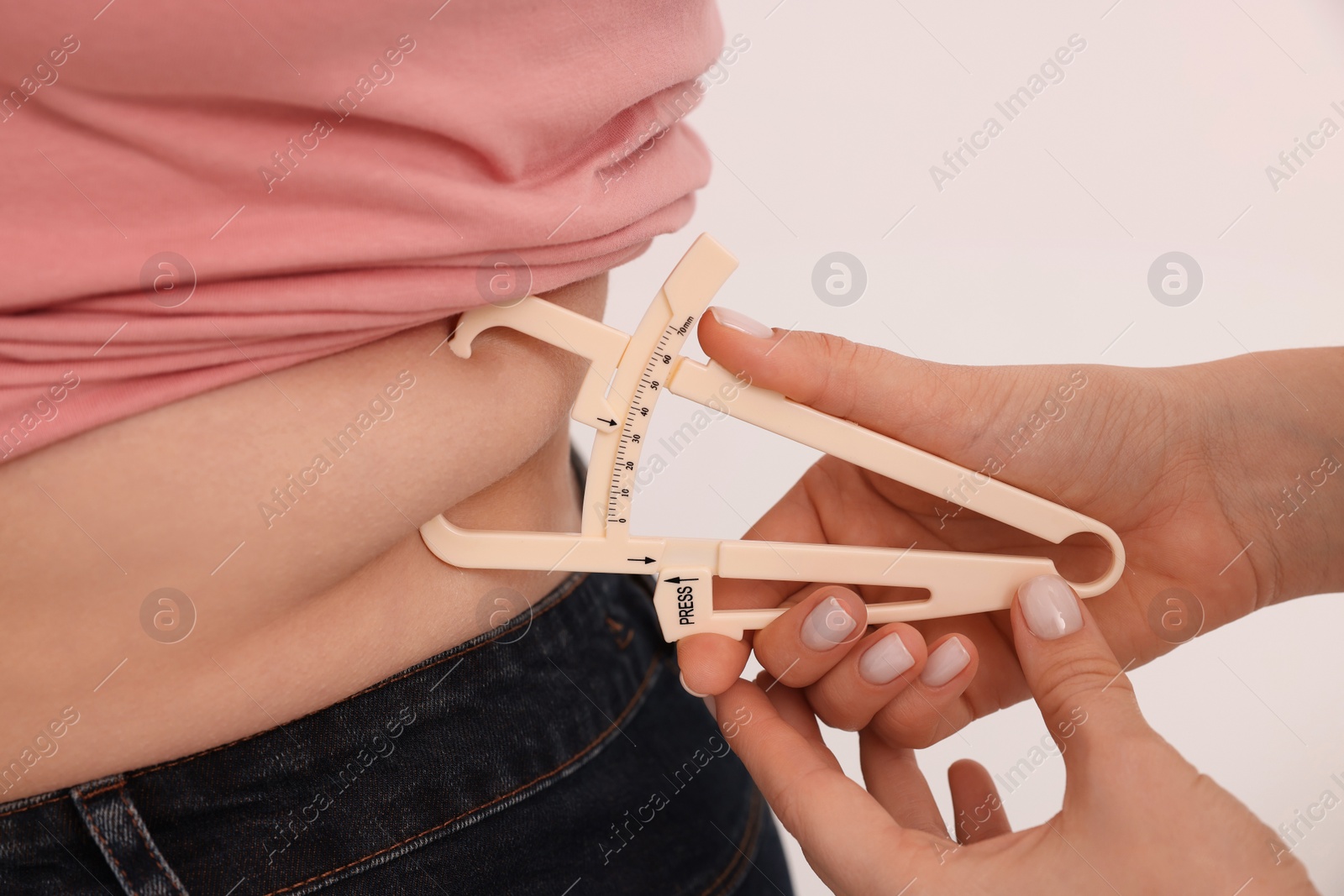 Photo of Nutritionist measuring overweight woman's body fat layer with caliper on white background, closeup