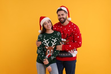 Photo of Happy young couple in Christmas sweaters and Santa hats on orange background