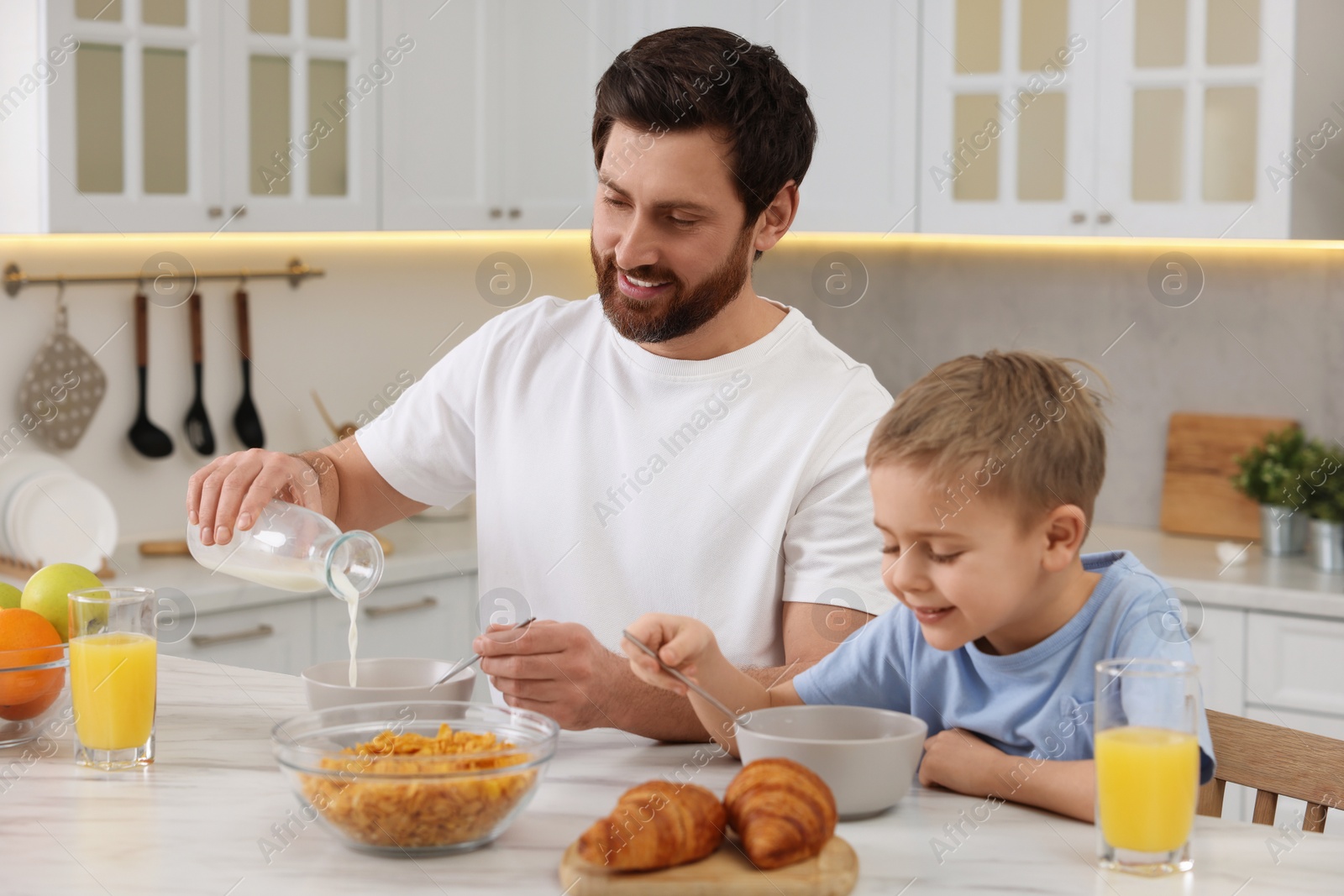 Photo of Father and his cute little son having breakfast at table in kitchen