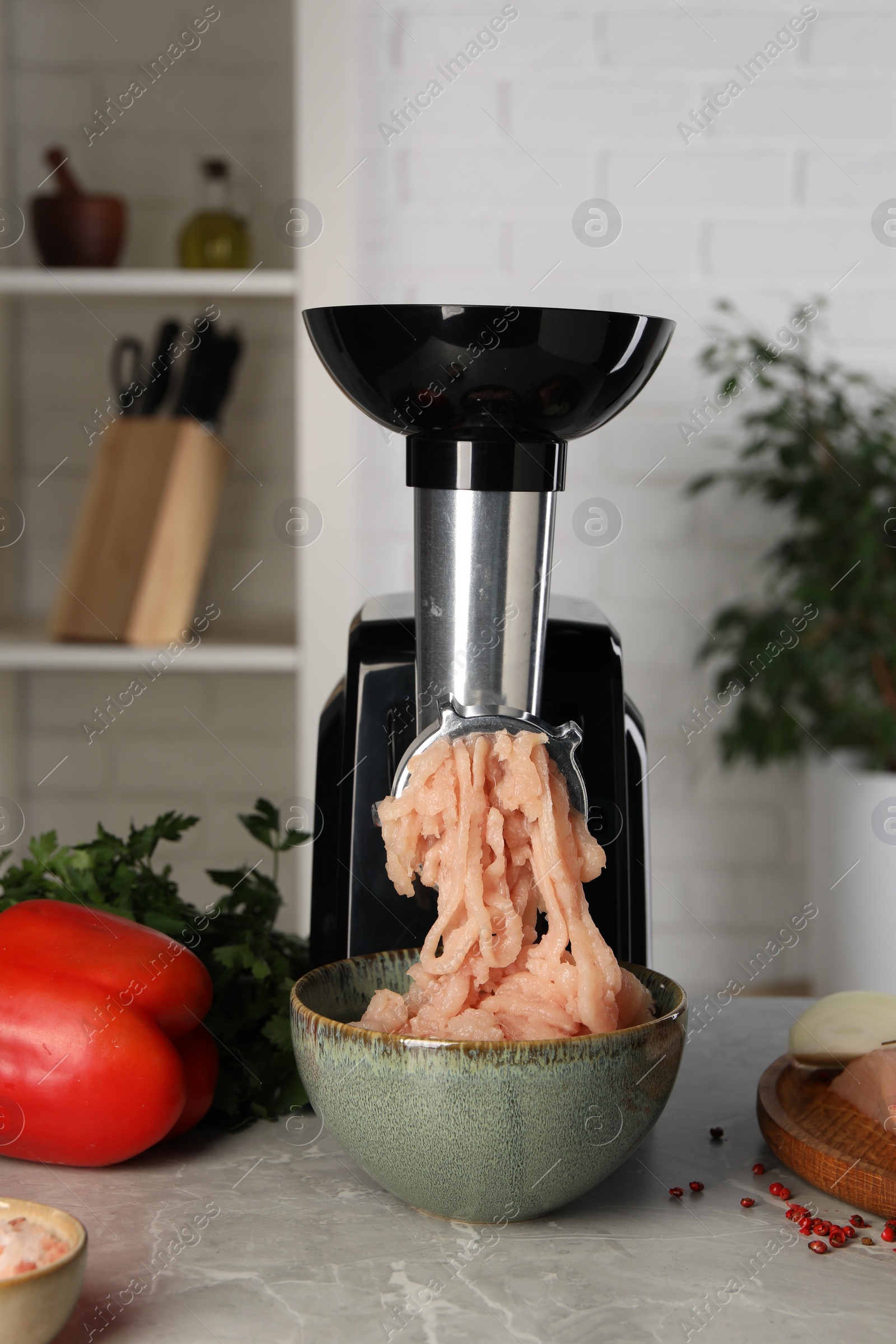 Photo of Electric meat grinder with chicken mince and products on grey marble table indoors