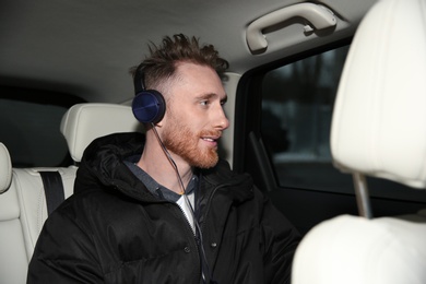 Photo of Young man listening to music with headphones in car