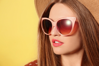 Image of Young woman wearing stylish sunglasses and hat on yellow background