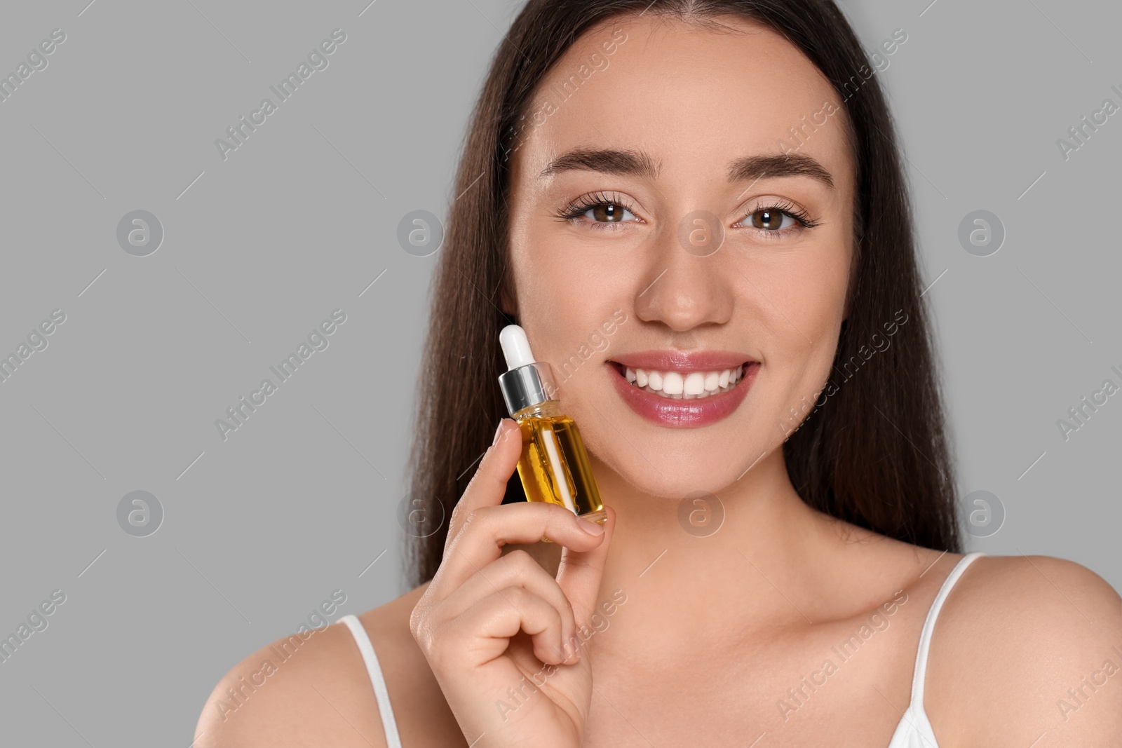 Photo of Beautiful young woman with bottle of essential oil on light grey background