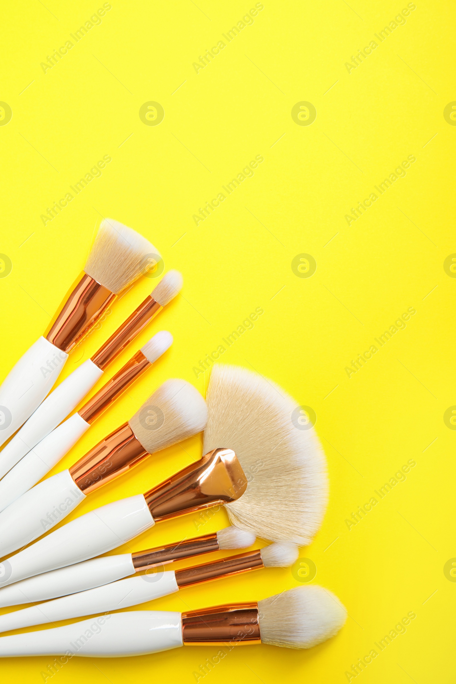 Photo of Flat lay composition with set of professional makeup brushes on yellow background. Space for text