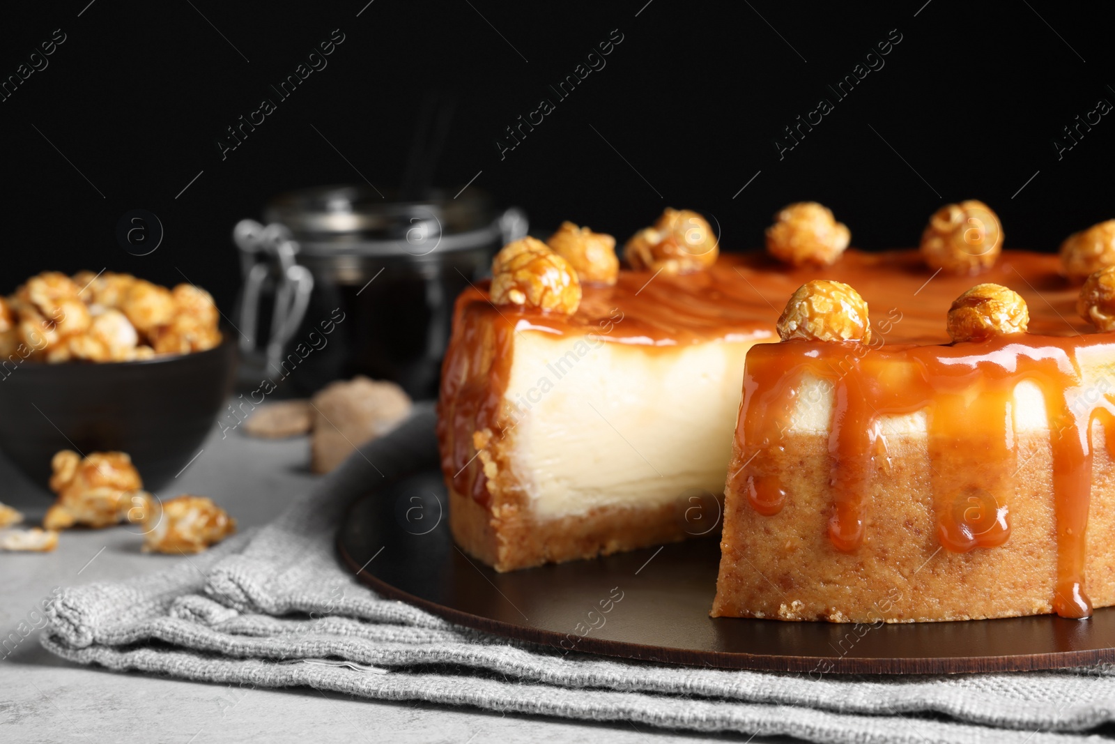 Photo of Sliced delicious cheesecake with caramel and popcorn on light grey table, closeup. Space for text