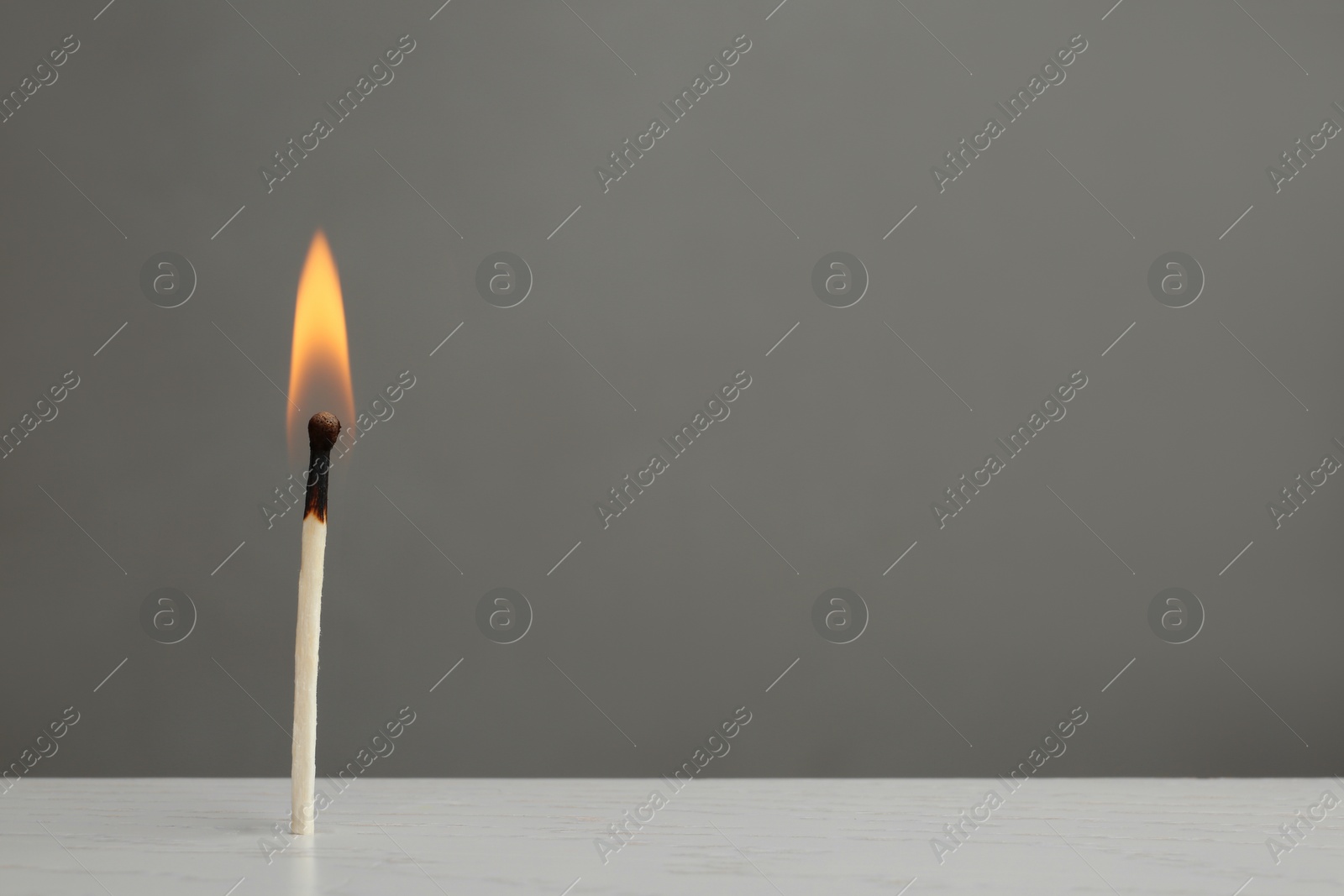 Photo of Lit match on table against grey background. Space for text