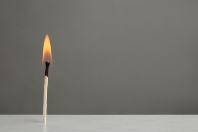 Photo of Lit match on table against grey background. Space for text