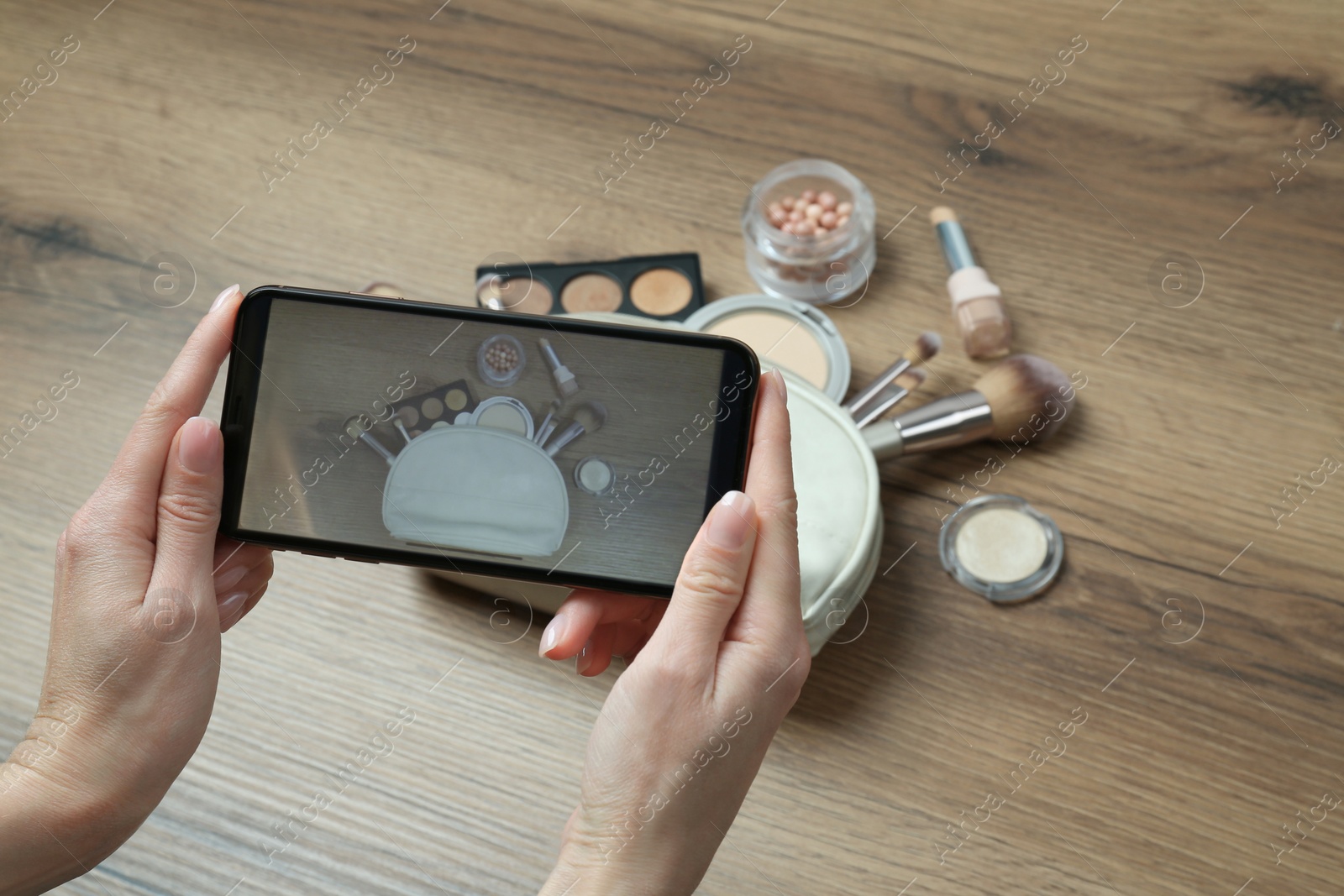 Photo of Woman taking photo of makeup products with smartphone at wooden table, closeup