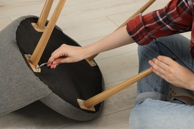 Photo of Woman with screwdriver assembling armchair on floor, closeup