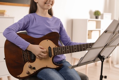 Photo of Little girl playing guitar at music lesson, closeup. Learning notes