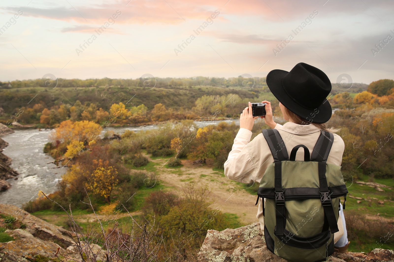 Photo of Traveler with backpack taking photos near mountain river, back view. Autumn vacation