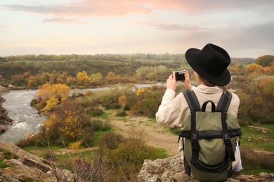 Photo of Traveler with backpack taking photos near mountain river, back view. Autumn vacation