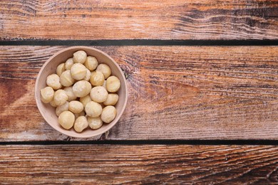 Photo of Delicious peeled Macadamia nuts in bowl on wooden table, top view. Space for text