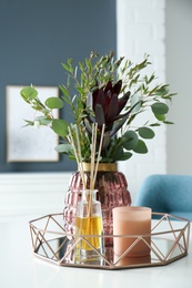 Photo of Beautiful bouquet with eucalyptus branches, candle and aromatic reed air freshener on white table indoors. Interior elements