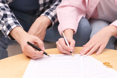 Man and woman signing marriage contract at wooden table indoors, closeup