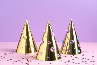 Photo of Golden party hats with bright rhinestones and confetti on color background