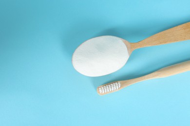 Bamboo toothbrush and wooden spoon with baking soda on light blue background, flat lay. Space for text
