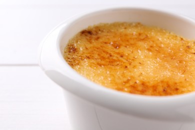 Photo of Delicious creme brulee in bowl on white table, closeup