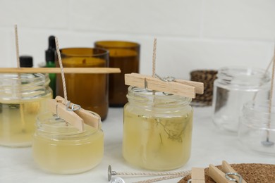 Photo of Glass jars with melted wax on white table. Handmade candles