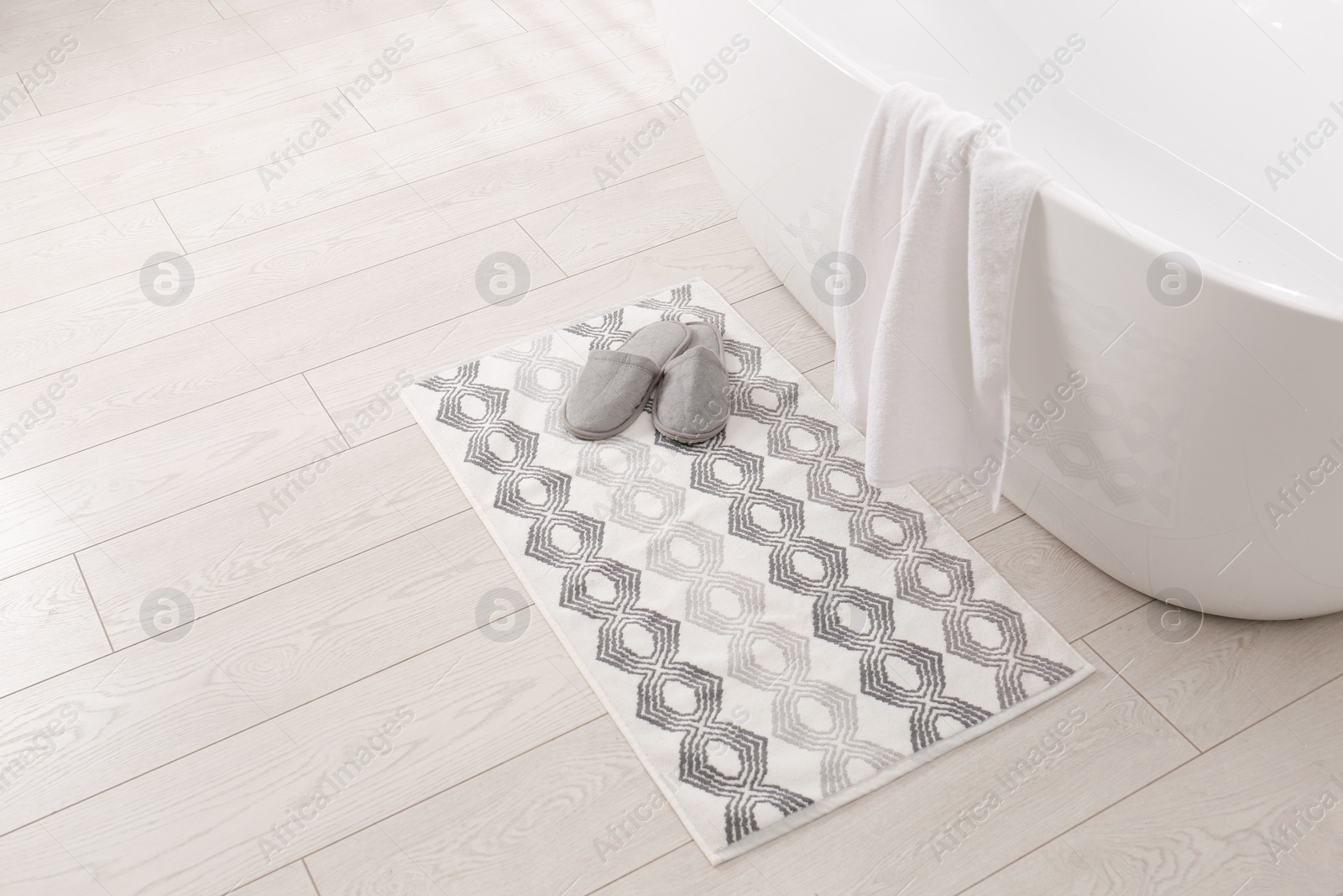 Photo of Soft bath mat and slippers on floor in bathroom