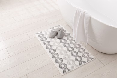 Photo of Soft bath mat and slippers on floor in bathroom