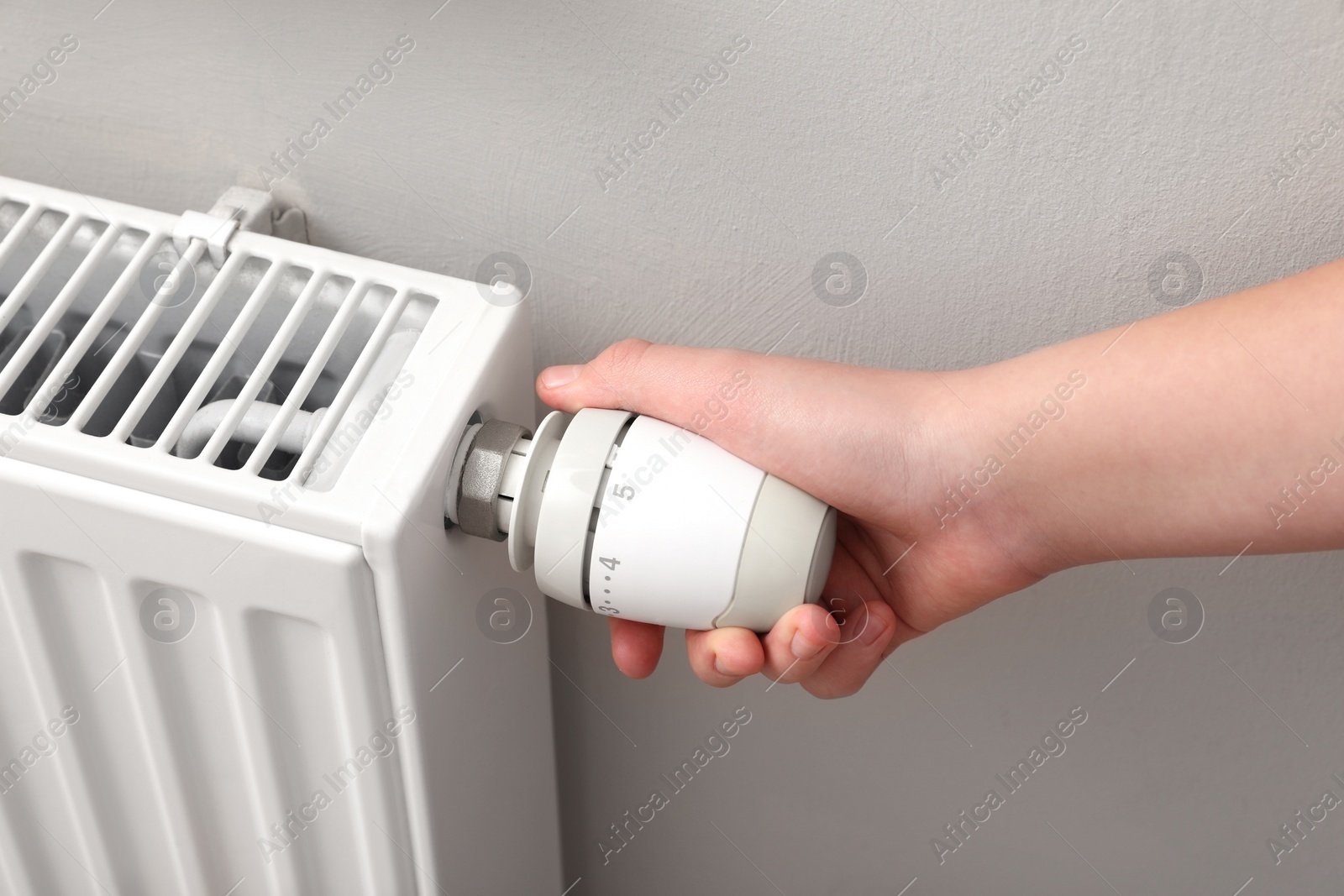 Photo of Girl adjusting heating radiator thermostat near white wall, closeup