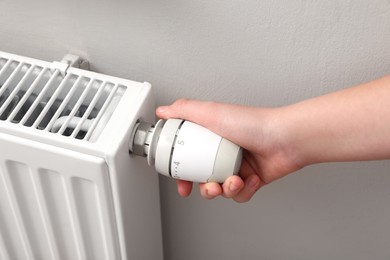 Photo of Girl adjusting heating radiator thermostat near white wall, closeup