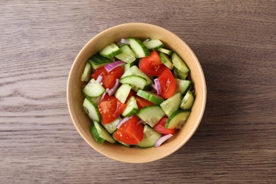 Bowl of vegetarian salad with cucumber, tomato and onion on wooden background, top view