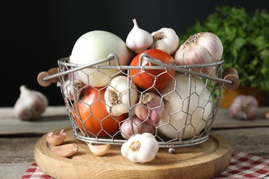 Fresh raw garlic and onions in metal basket on table, closeup