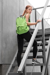 Beautiful woman in gym clothes posing with stylish backpack on stairs on street