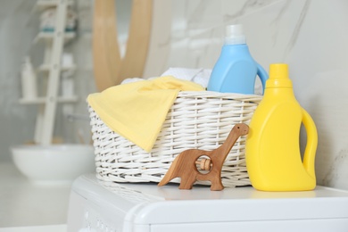 Bottles of detergent, children's clothes and toy on washing machine in bathroom