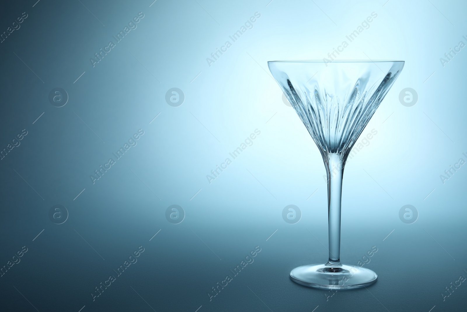 Photo of Elegant empty martini glass on light blue background. Space for text