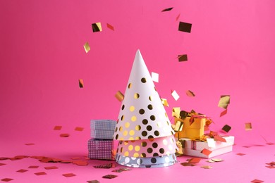 Photo of Party hats, gift boxes and confetti on pink background