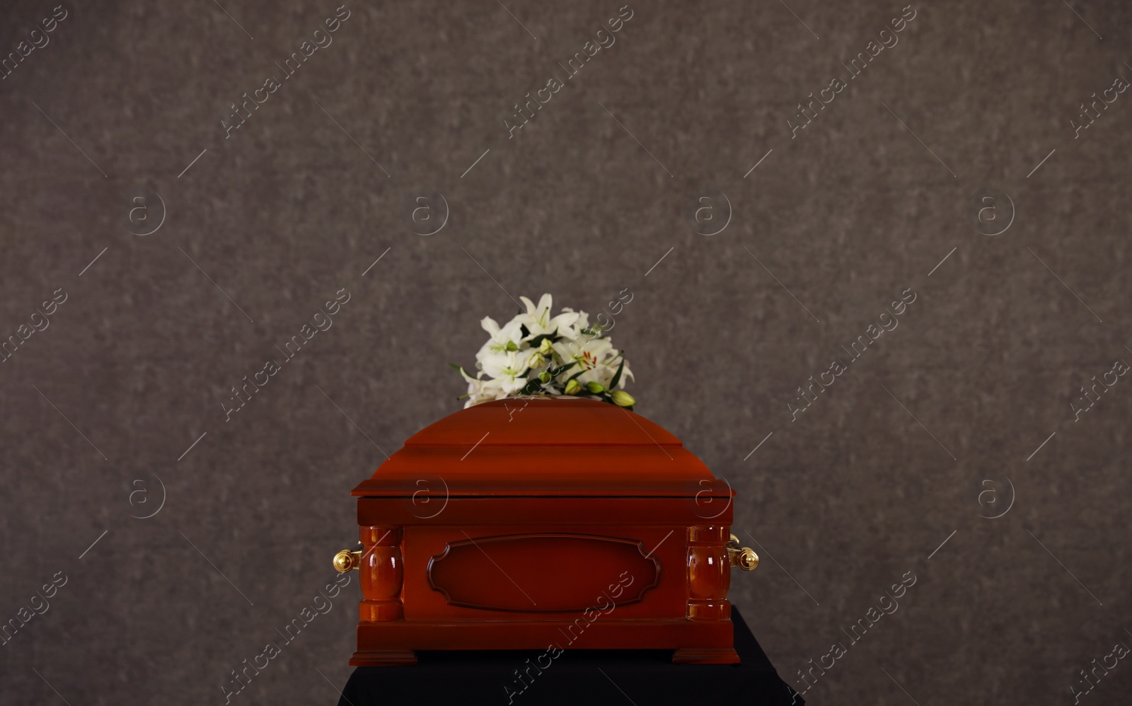 Photo of Wooden funeral casket with white lilies at grey wall