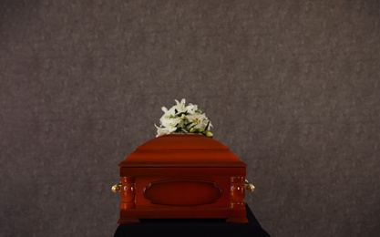 Wooden funeral casket with white lilies at grey wall