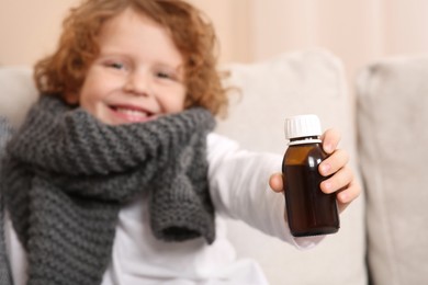 Photo of Cute boy holding bottle with cough syrup on sofa, focus on hand. Effective medicine